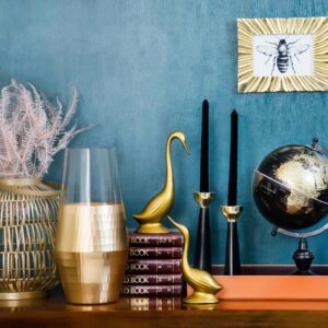 Stylish home decor arrangement including a globe, books, candles, and vases on a blue backdrop.