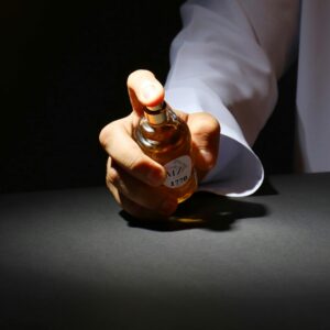 A hand elegantly holding a perfume bottle against a dark backdrop, highlighting luxury fragrance.