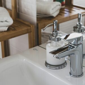 Elegant bathroom featuring a chrome faucet and soap dispenser, with a wooden shelf and plush towels.
