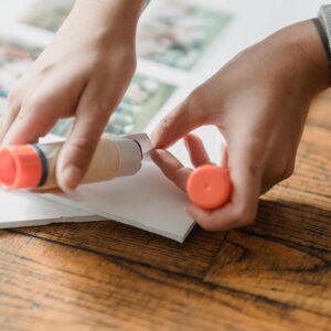 Crop anonymous person gluing set of photos to poster on wooden surface in daylight