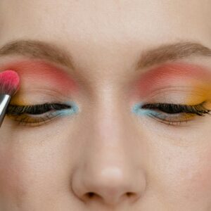Vibrant eye makeup close-up with brush applying pink, blue, and yellow colors.