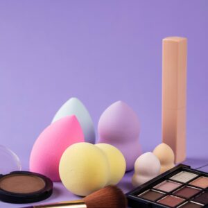 A collection of beauty blenders and makeup products on a purple background.