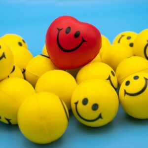 Red heart-shaped ball among yellow smiley faces on a blue background.
