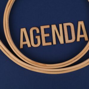 Wooden letters form the word 'AGENDA' encircled by hoops on a blue surface, suggesting planning and strategy.