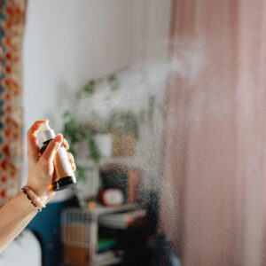 A hand spraying room freshener in a cozy home interior with ethnic decor and natural light.
