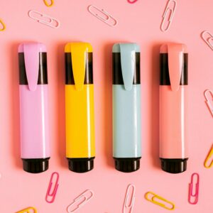 A flat lay of colorful markers and paper clips on a pink surface, perfect for stationery themes.