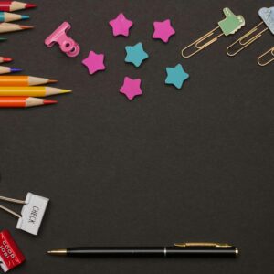 A vibrant flat lay of art supplies on a dark backdrop, featuring pencils and paper clips.