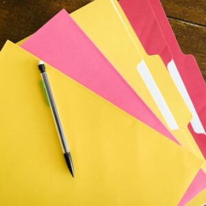 Colorful folders and pen arranged on a wooden table for office organization.