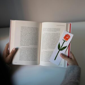 A person holding an open book with a floral bookmark, depicting reading and relaxation.