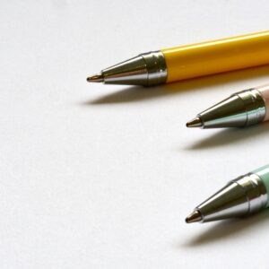 Three multicolored ballpoint pens lay on a clean white surface in a minimal style.