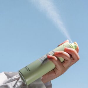 Person's hand spraying deodorant in front of a clear sky, product shot.