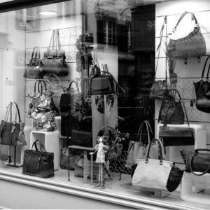 Black and white photo of a boutique window showcasing luxury handbags on display.