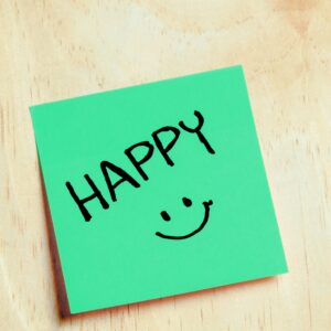 pexels-photo-34981845-34981845 Green sticky note with handwritten 'HAPPY' and smiley face on wooden surface.