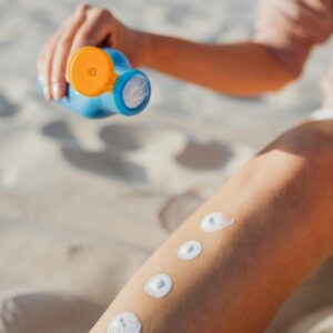 Woman applying sunscreen lotion on leg at the beach. Summer skincare routine for sun protection outdoors.