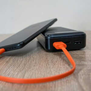 A smartphone charging via an orange cable connected to a power bank on a wooden surface.