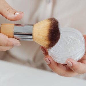 Close-up view of a hand applying face powder with a makeup brush, perfect for beauty and lifestyle concepts.