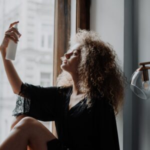 pexels-photo-4153787-4153787 Young woman with curly hair using a spray bottle by a window, embracing natural beauty and self-care.